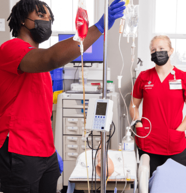 两名身穿圣医院红色工作服的学生在护理实验室使用设备