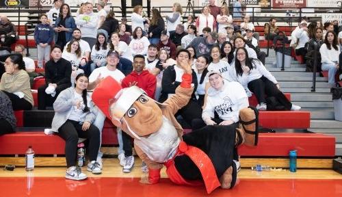 Marty the Mascot poses with a group of students in bleachers at Pack the Pavilion