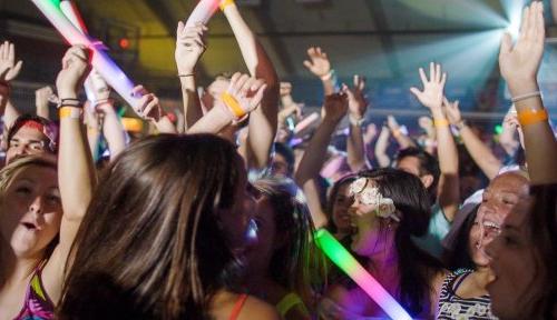 A large group of students dance with glowsticks, their hands in the air