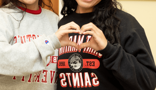 两名身穿新大运动衫的学生用手做了一个心形图案
