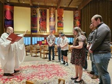 Fr. 彼得穿着宗教长袍，对着一群低着头围成半圆形的学生朗读